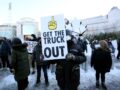 A protester holds a sign with a raised middle finger and the words “get the truck out.”
