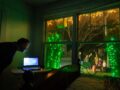 A man looks at a computer next to a picture window out to his decorated yard.