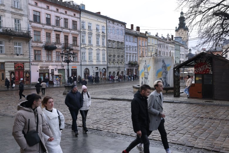 People in winter clothing walk on cobblestone paths in a square flanked by colourful buildings.