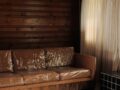 A photo of a plastic-covered brown couch, a wooden wall and white curtains in the background.