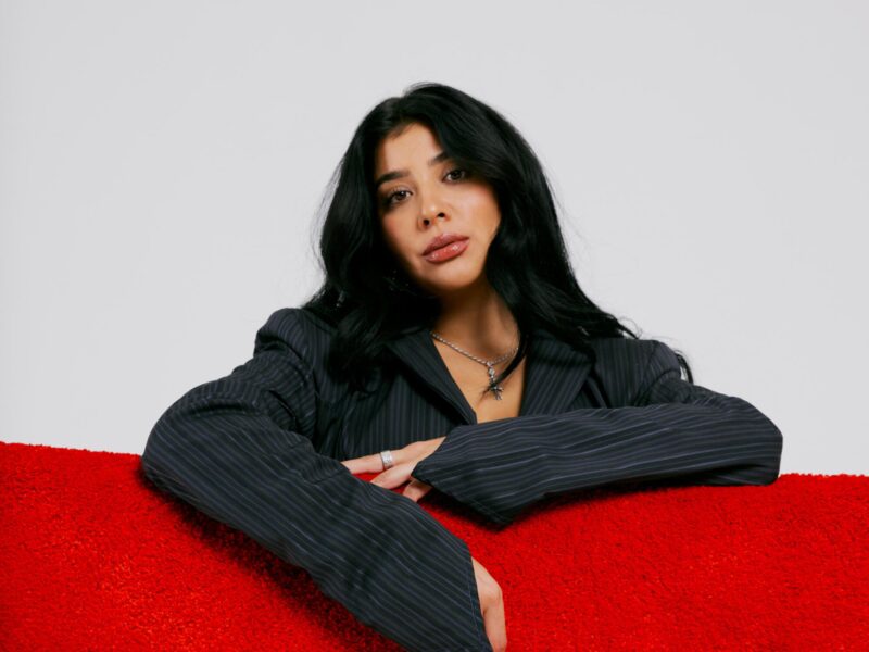 A woman wearing a dark gray suit leans against a red cushion.